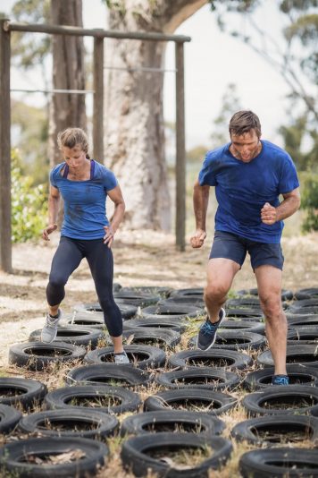 Man and woman running over the tyre during obstacle course in boot camp